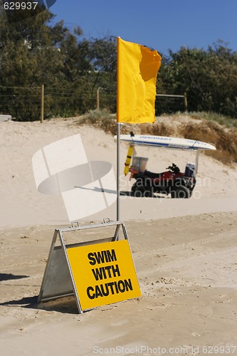 Image of Swimming caution sign and flag on beach.
