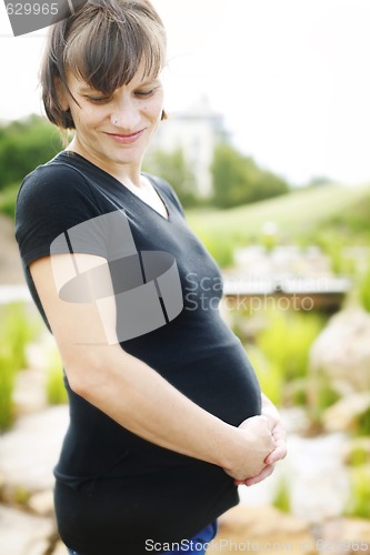 Image of Happy pregnant woman holding her belly while outdoors.