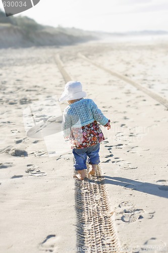 Image of Little girl walking along a tire track on a beach. 
