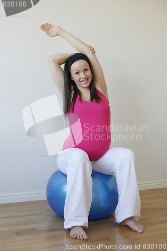 Image of Young pregnant woman doing stretching exercise sitting on fitnes