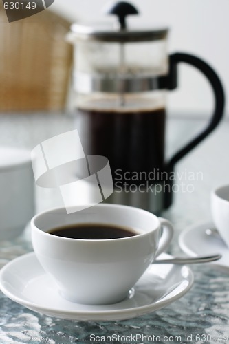 Image of Black filter coffee and plunger on a glass table.