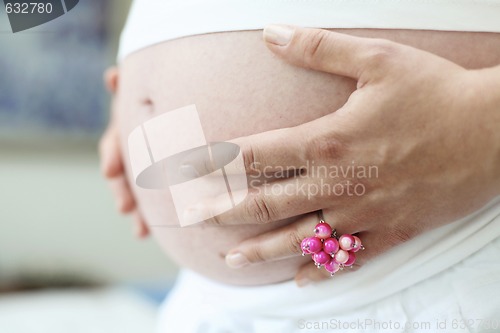 Image of Woman holding her bare pregnant belly indoors.