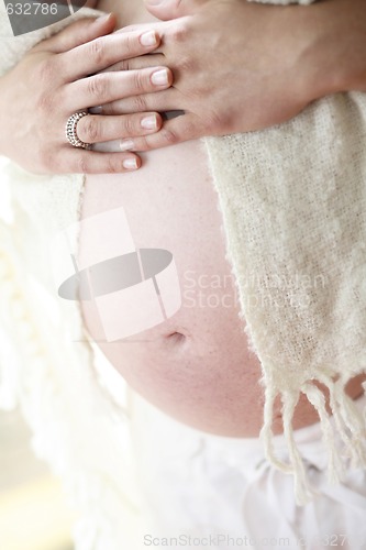 Image of Woman holding her bare pregnant belly indoors.