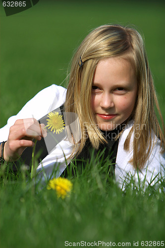 Image of blonde girl smiling and lies in the grass with a flower