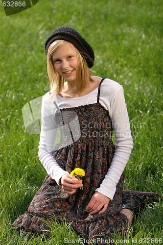 Image of blonde girl smiling and lies in the grass with a flower