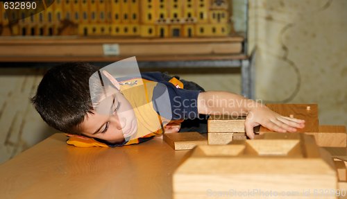 Image of Cute little boy plays with wooden bricks and builds a house