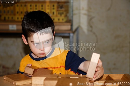 Image of Cute little boy plays with wooden bricks and builds a house