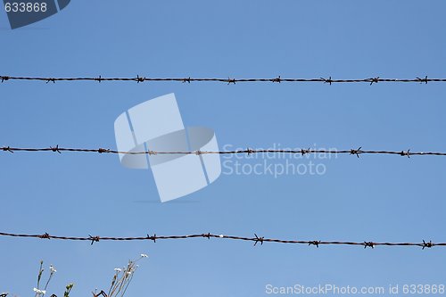 Image of Three rusty strands of barbed wire over blue sky background