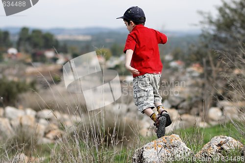 Image of Little boy jumps from the stone outdoors