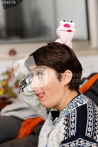 Image of Young woman with a doll on her head sticks out her tongue 