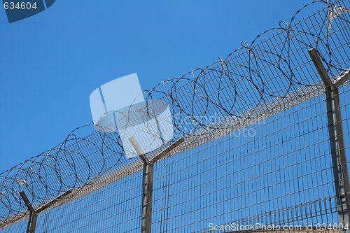 Image of Fence with spiral barbed wire on top on sky background