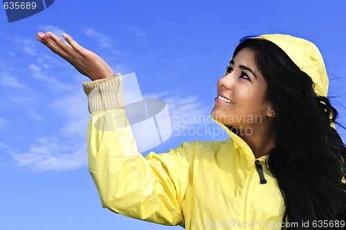 Image of Beautiful young woman in raincoat checking for rain