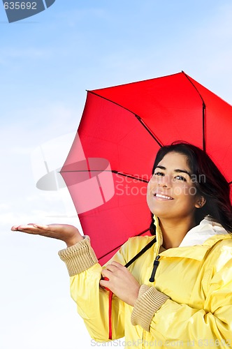 Image of Beautiful young woman in raincoat with umbrella checking for rain