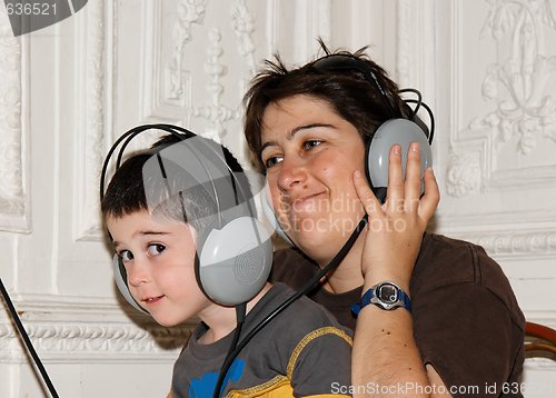 Image of Cute little boy listens to music in earphones with his mother 