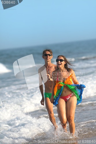 Image of happy couple running along the beach on summer day