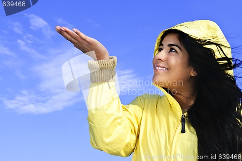 Image of Beautiful young woman in raincoat checking for rain