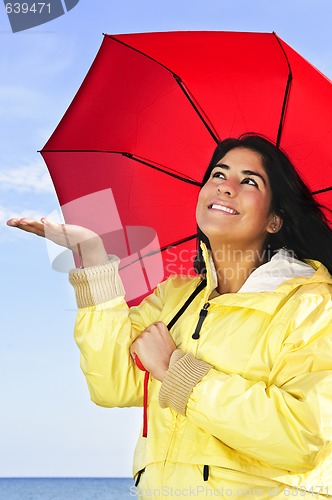 Image of Beautiful young woman in raincoat with umbrella checking for rain