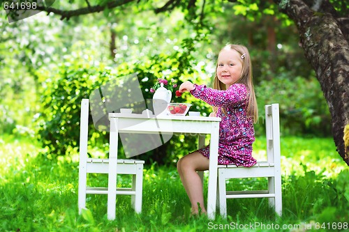 Image of Smiling little girl holding a strawberry at tea party. 