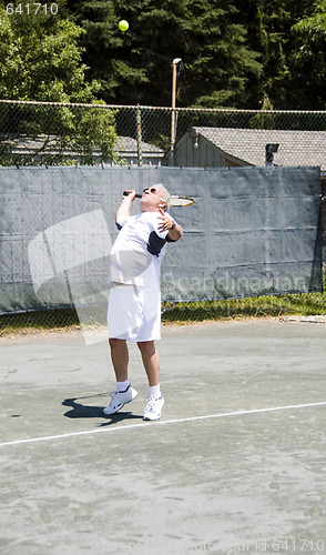 Image of middle age tennis player serving the ball on court