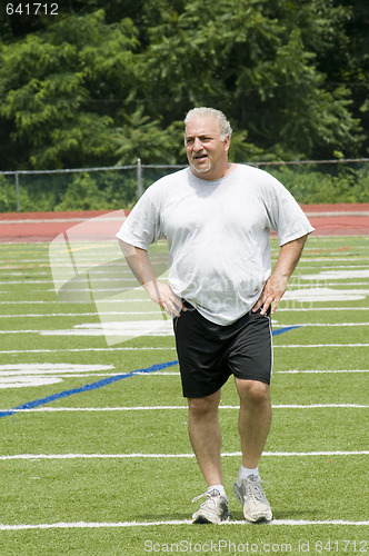 Image of middle age man stretching and exercising on sports field