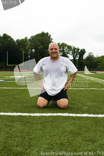 Image of middle age man stretching and exercising on sports field