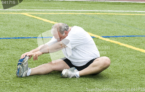 Image of middle age man stretching and exercising on sports field