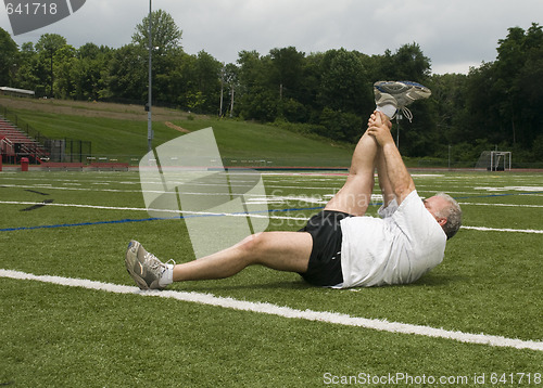 Image of middle age man stretching and exercising on sports field