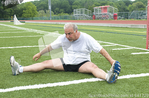 Image of middle age man stretching and exercising on sports field