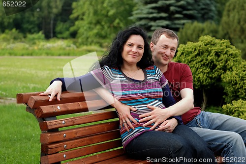 Image of Young happy couple (pregnant woman) on bench