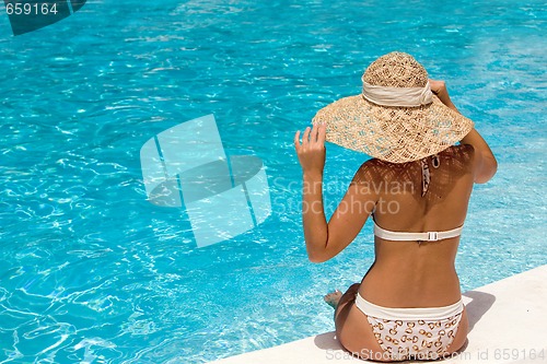 Image of Woman in hat relaxing beside the pool