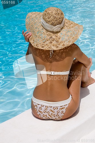 Image of Woman in hat relaxing beside the pool