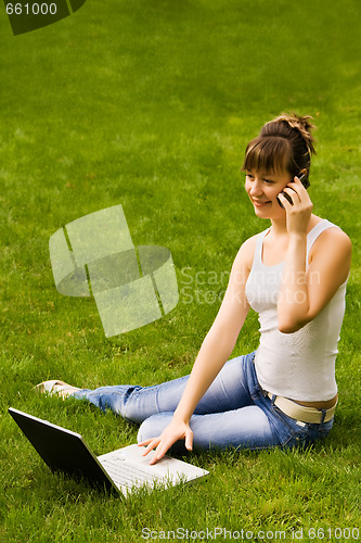 Image of Happy young woman with notebook and mobile phone on the grass