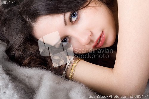 Image of Lovely young woman lying on grey fur coat