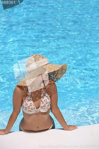 Image of Woman in hat relaxing beside the pool