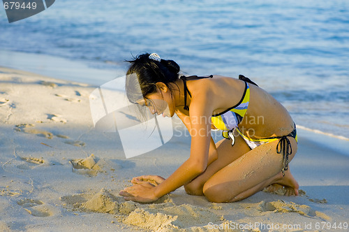 Image of beautiful young woman playing with the sand