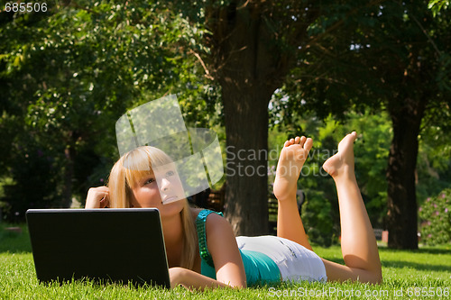 Image of Young thoughtful girl on the grass with notebook looks at the sky