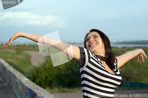 Image of Happy young woman with arms raised outdoors