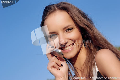 Image of pretty smiling young woman talking on mobile outdoors in summer