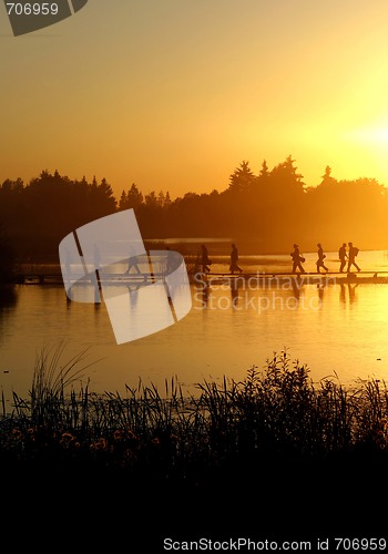 Image of A group of people walking on the footpath on the lake at sunset
