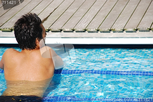 Image of Young man relaxing at the edge of the swimming pool