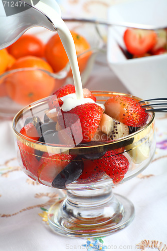 Image of Cream being poured on Fresh fruit salad in a glass bowl