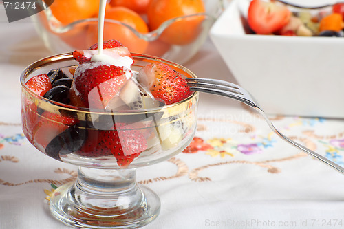 Image of Cream being poured on Fresh fruit salad in a glass bowl