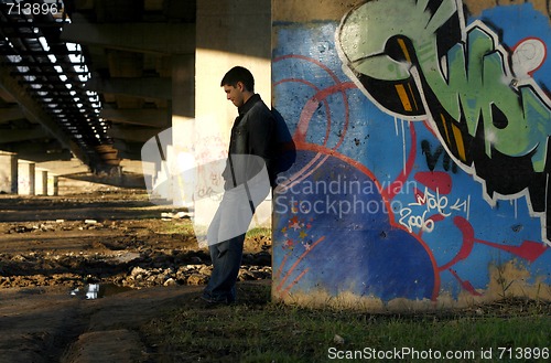 Image of Young handsome man leaning against the bridge column with colorf