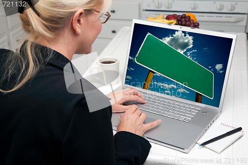 Image of Woman In Kitchen Using Laptop with Blank Road Sign on Screen