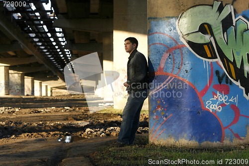 Image of Young handsome man leaning against the bridge column with colorf