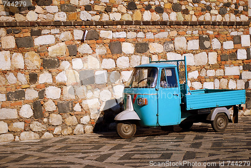 Image of Blue tricycle scooter in front of stone wall