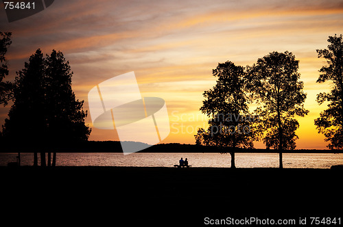 Image of Elderly couple sitting on a bench by lake at sunset