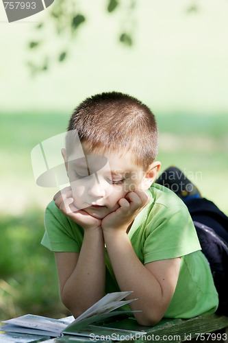 Image of Little boy reading book in park