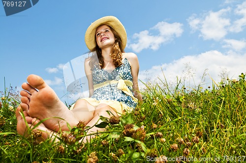 Image of Young barefoot girl sitting in meadow