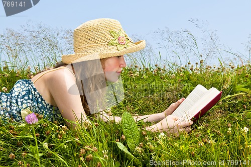 Image of Young girl reading book in meadow